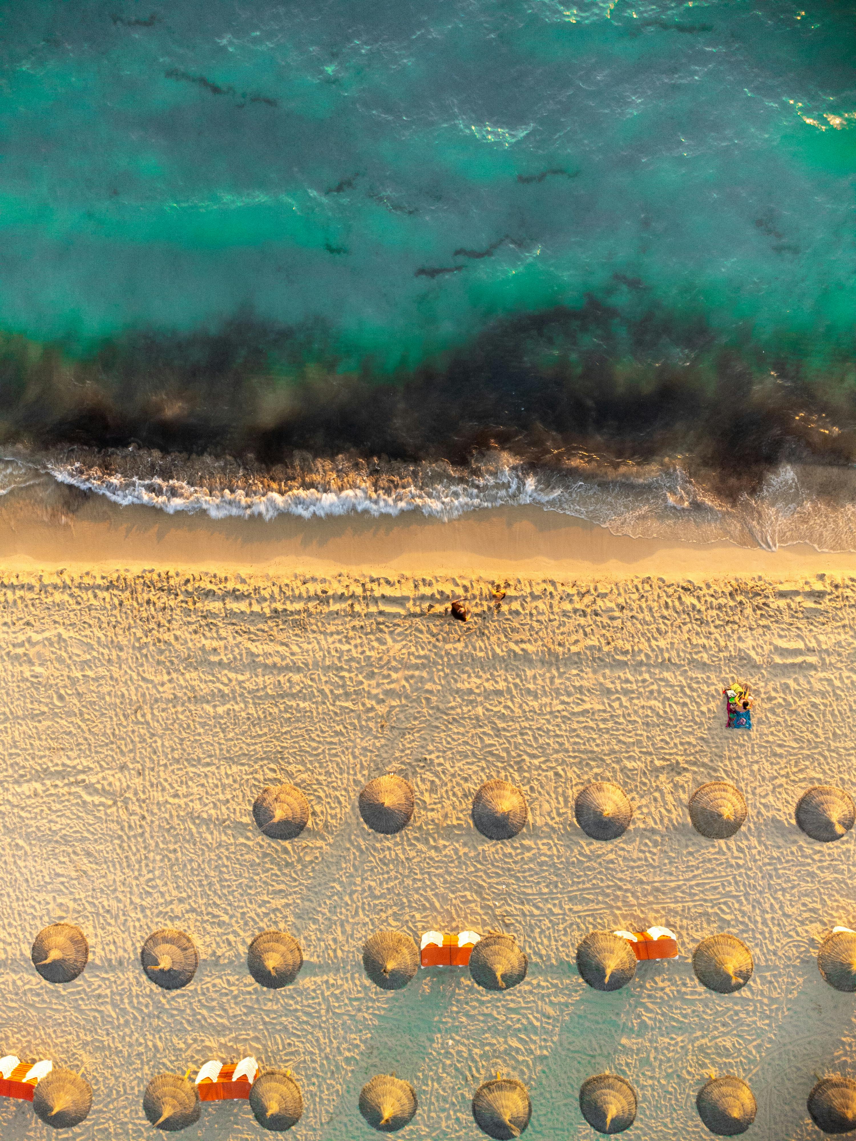 无人机拍摄了海滩，上面有稻草伞和碧绿色的波浪