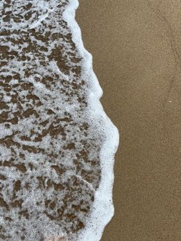 Calming image of ocean waves gently washing onto a sandy beach shore in natural light.