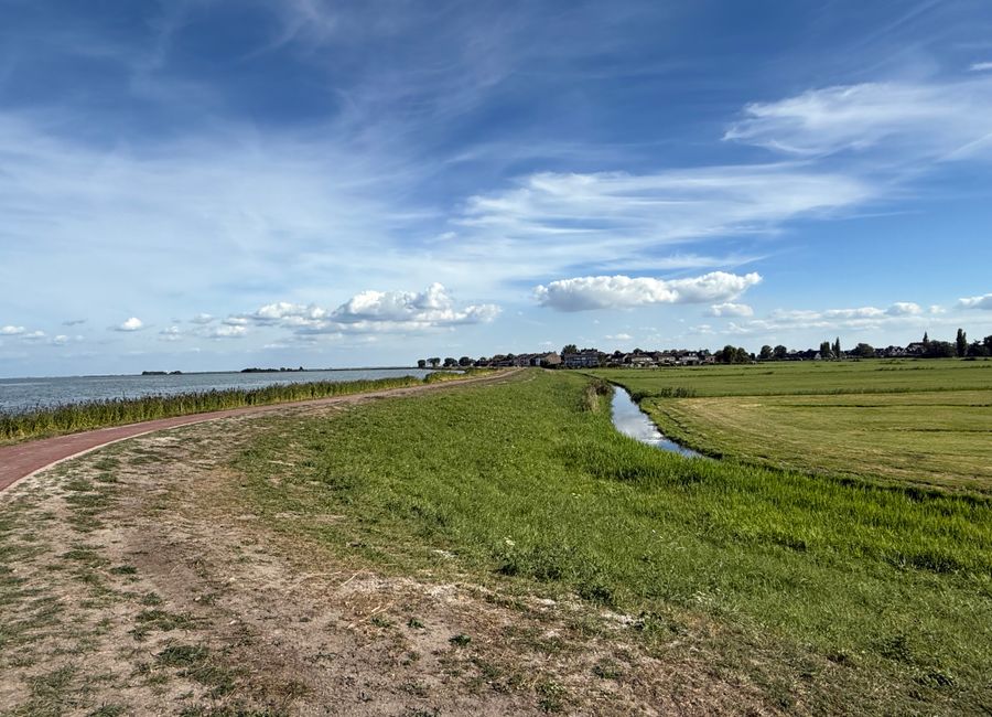 Peaceful scene of Dutch countryside with fields and a canal under a bright blue sky.