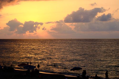 Free A tranquil sunset over a beach with silhouetted people and umbrellas. Stock Photo