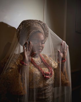 Woman in traditional attire with veil, accented by red jewelry, captured indoors with a warm and vibrant mood.