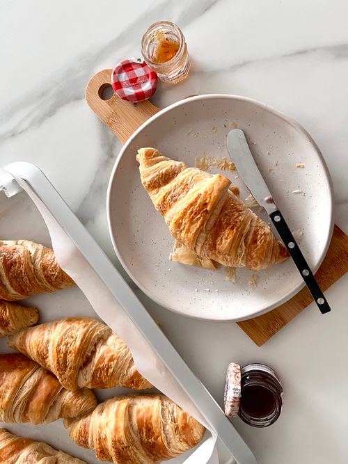 Free Delicious fresh croissants on a plate with small jam jars on a marble countertop. Stock Photo