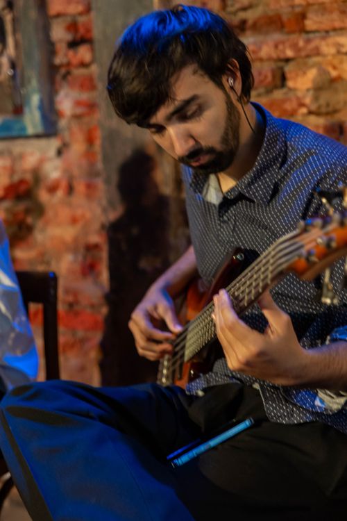 Free Young adult playing bass guitar in Mar del Plata, Argentina with a rustic brick wall backdrop. Stock Photo