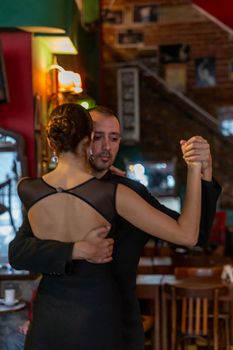 A couple gracefully dances tango in a cozy Buenos Aires cafe setting.