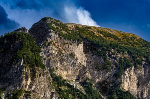 Free Stunning view of a rugged mountain peak with lush greenery under a blue sky with clouds. Stock Photo