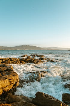 Stunning coastal scene with waves crashing on rocky shore under a serene blue sky.