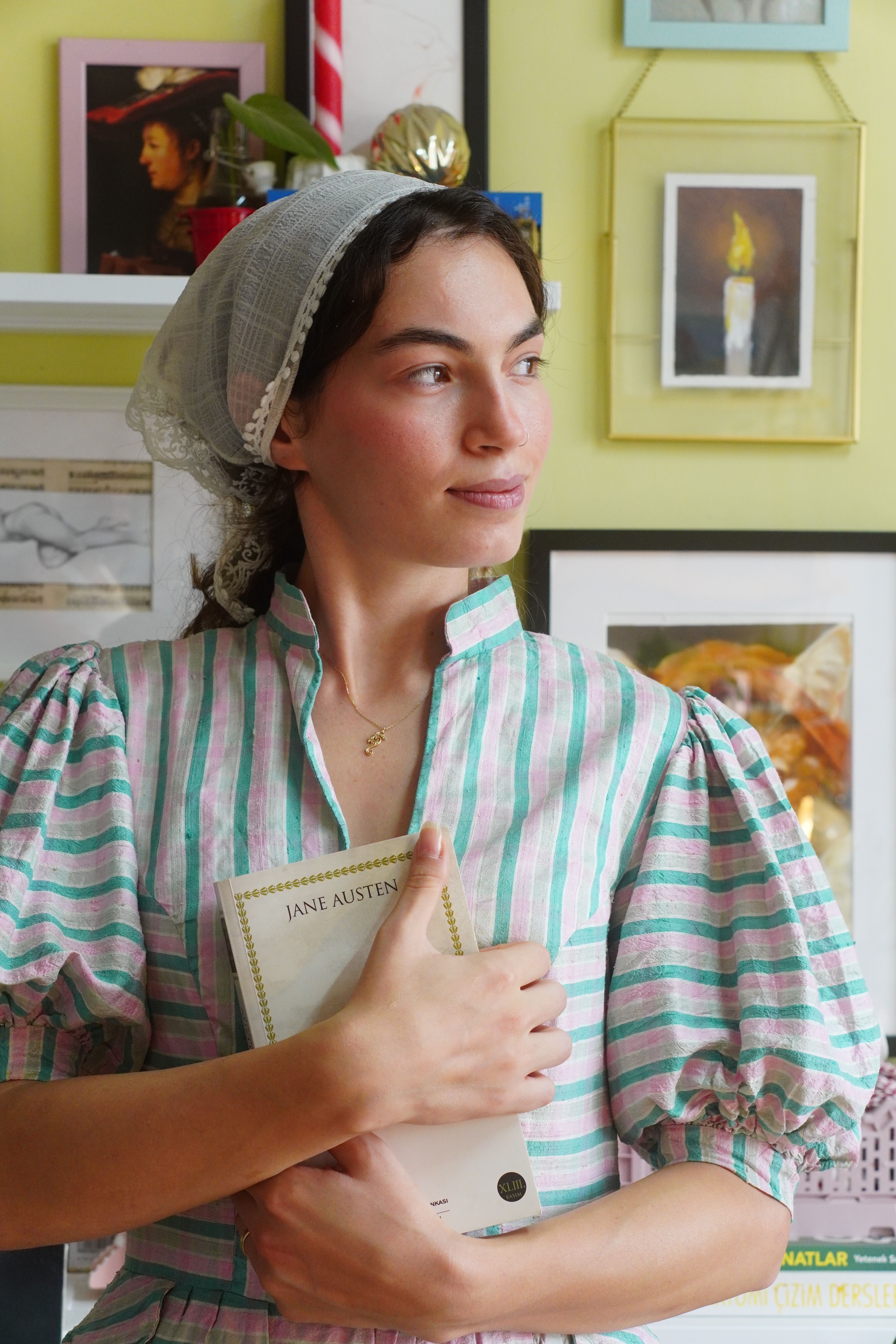 Woman in vintage attire holding a Jane Austen book, gazing thoughtfully indoors.