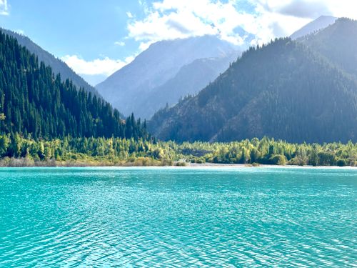 Free Beautiful turquoise lake surrounded by mountains and forests in Kazakhstan, under a clear blue sky. Stock Photo