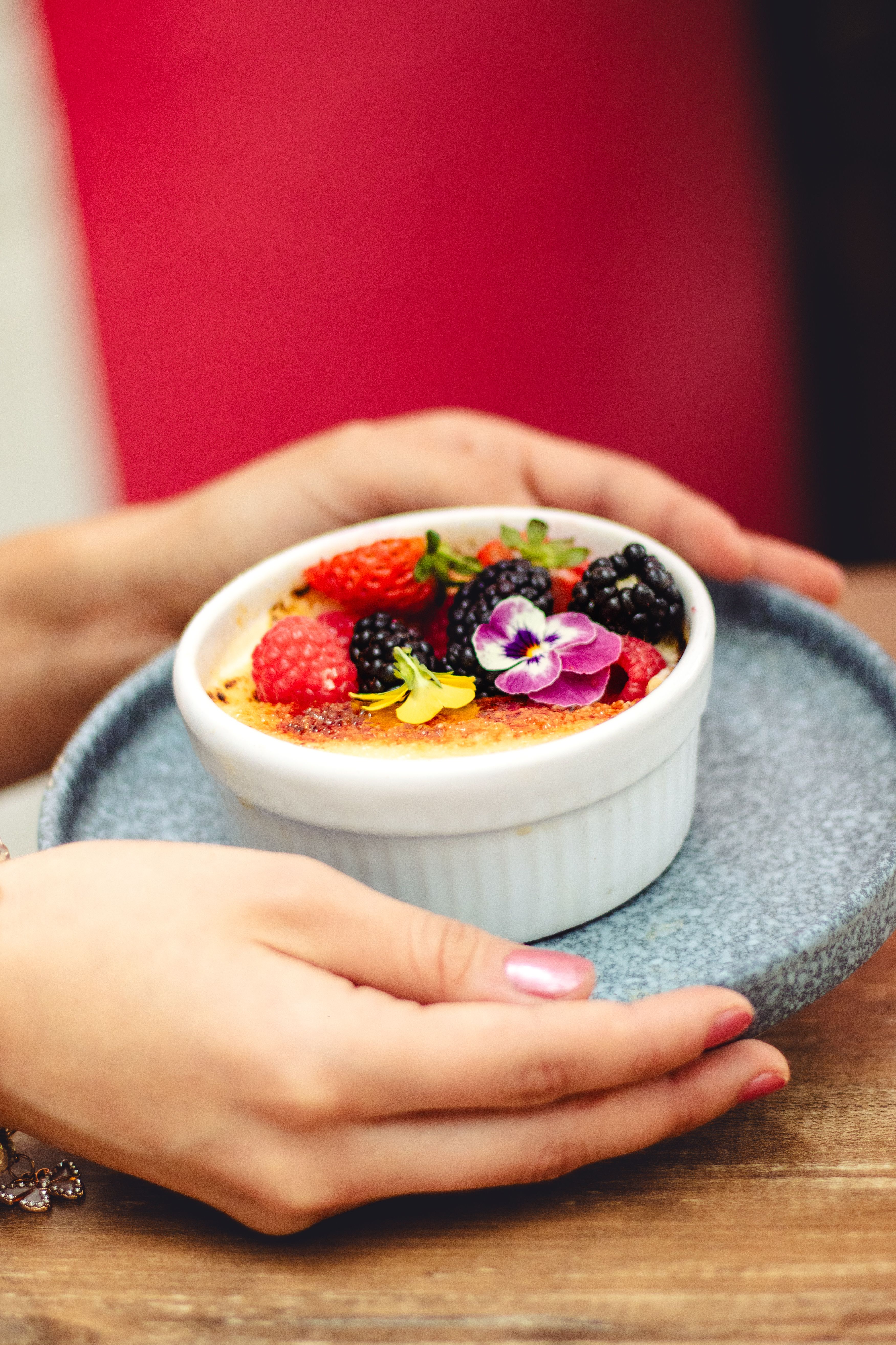 Elegant creme brulee garnished with fresh berries and a flower, served on a wooden table.