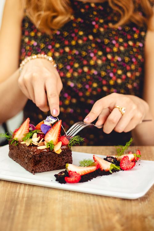 Free Delicious chocolate cake topped with fresh strawberries, raspberries, and edible flowers on a white plate. Stock Photo