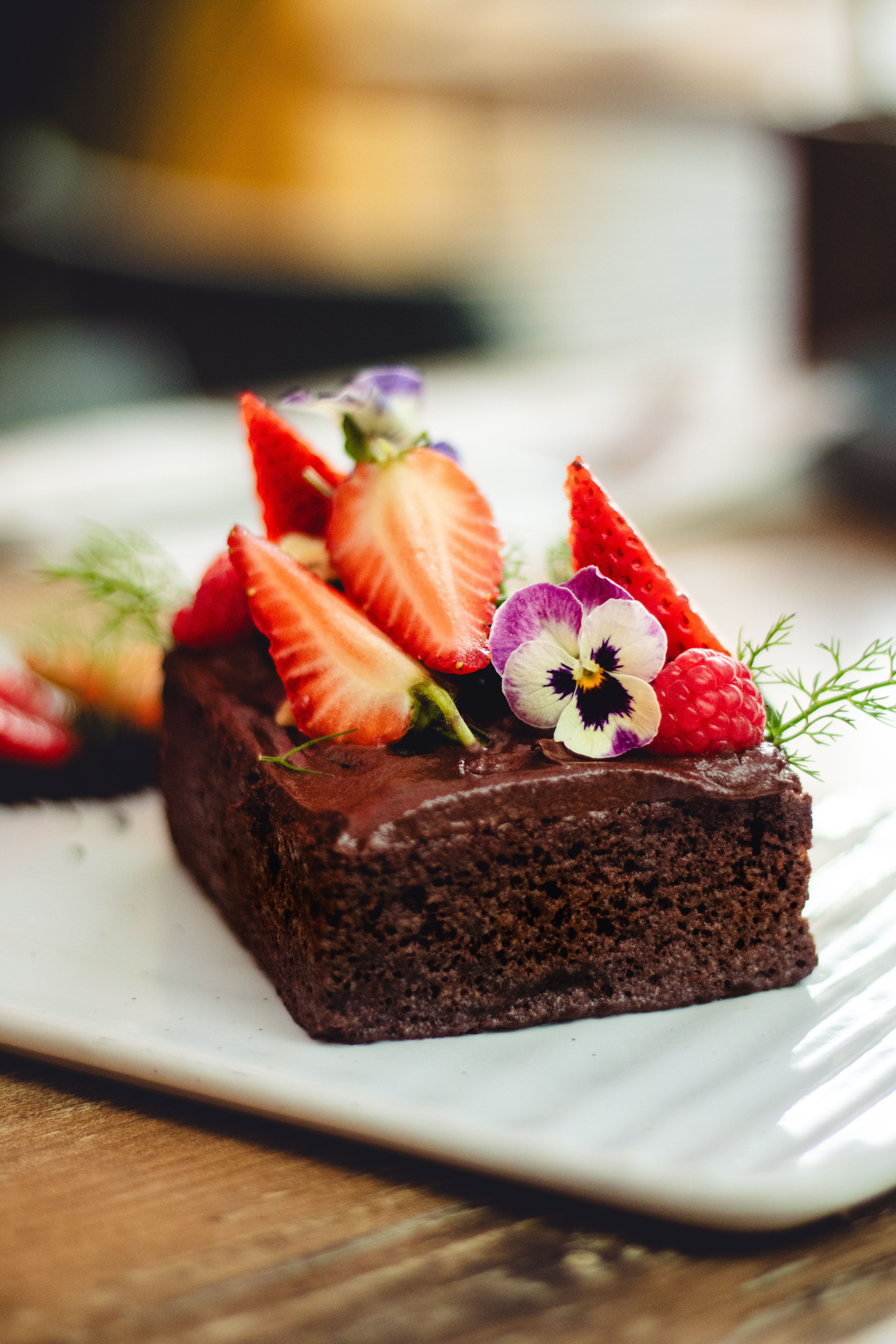 Close-up of a chocolate cake garnished with strawberries, raspberries, and flowers.