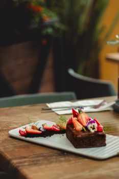 A beautifully styled chocolate cake topped with fresh strawberries and edible flowers on a rustic table.