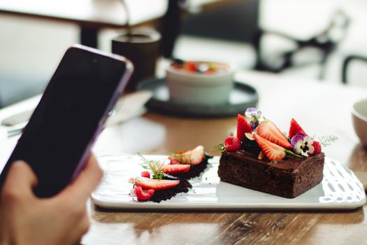 Artfully arranged chocolate dessert garnished with fresh strawberries and edible flowers, captured indoors.