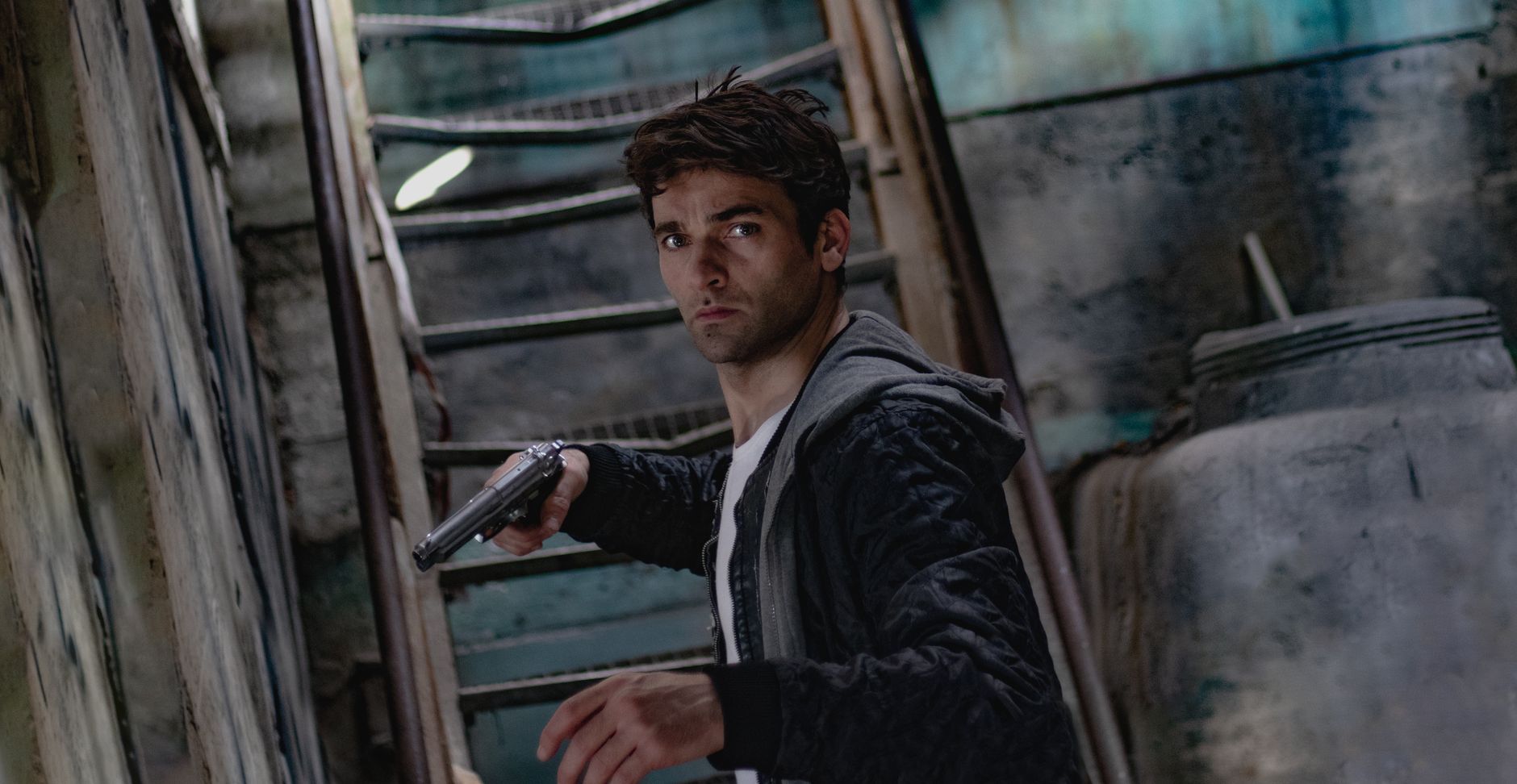 A man holding a gun in a dimly lit, mysterious urban setting.