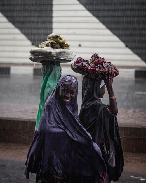 Free Women with headscarves and goods on heads walk through a rainy market street. Stock Photo