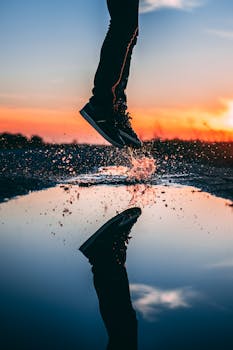 一个人跳过水坑，倒映出充满活力的日落天空，激起一片动态的水花