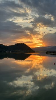 A breathtaking sunset over a tranquil lakeside, reflecting vibrant orange and yellow hues in the water, creating a peaceful atmosphere.