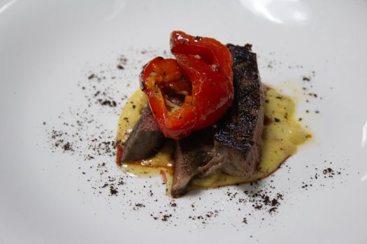 Gourmet grilled steak with roasted red pepper served on a white plate, showcasing fine dining cuisine.