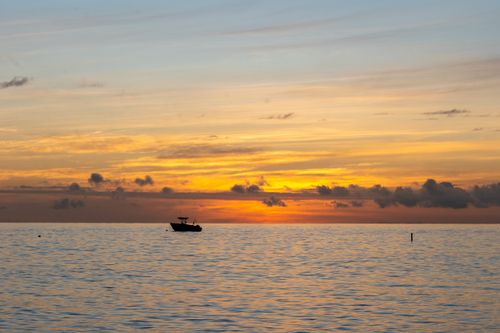 Free A beautiful ocean sunset with a silhouetted boat on the horizon, creating a tranquil scene. Stock Photo