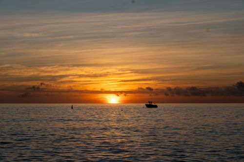 Free A tranquil sunset over the ocean with a silhouette of a boat, offering a stunning view. Stock Photo