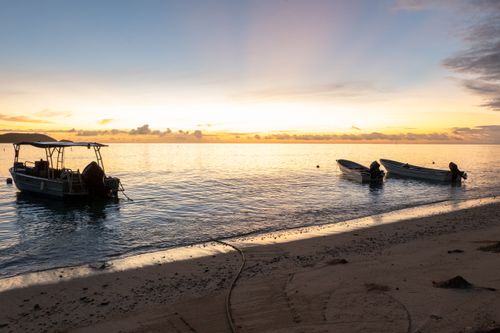 Free Serene sunrise at a tropical beach in Fiji, featuring boats gently floating at the shore. Stock Photo