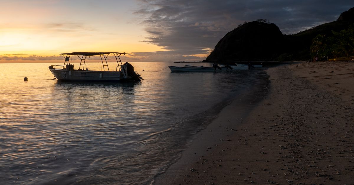 Serene sunrise over a tranquil Fijian beach with a boat, capturing a peaceful island life.