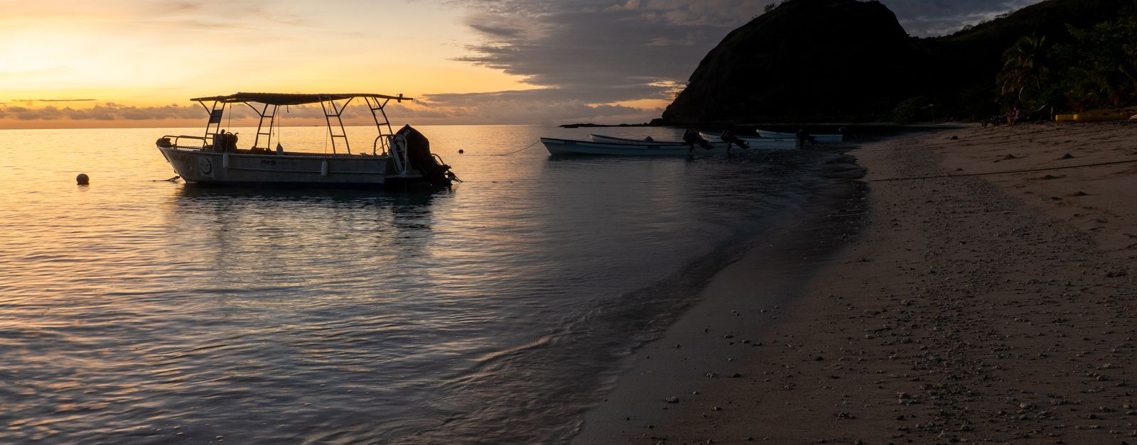 Serene sunrise over a tranquil Fijian beach with a boat, capturing a peaceful island life.