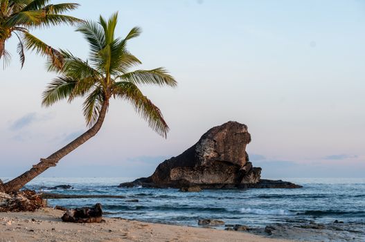 Peaceful sunrise view of a pristine beach on Kuata Island with palm trees and coastal rock formations.
