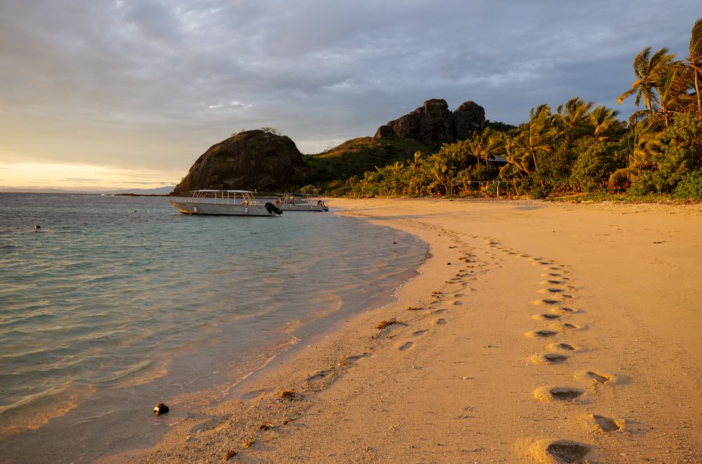 Playa privada de las islas Yasawa en Fiji con bote al ocaso y huellas en la arena