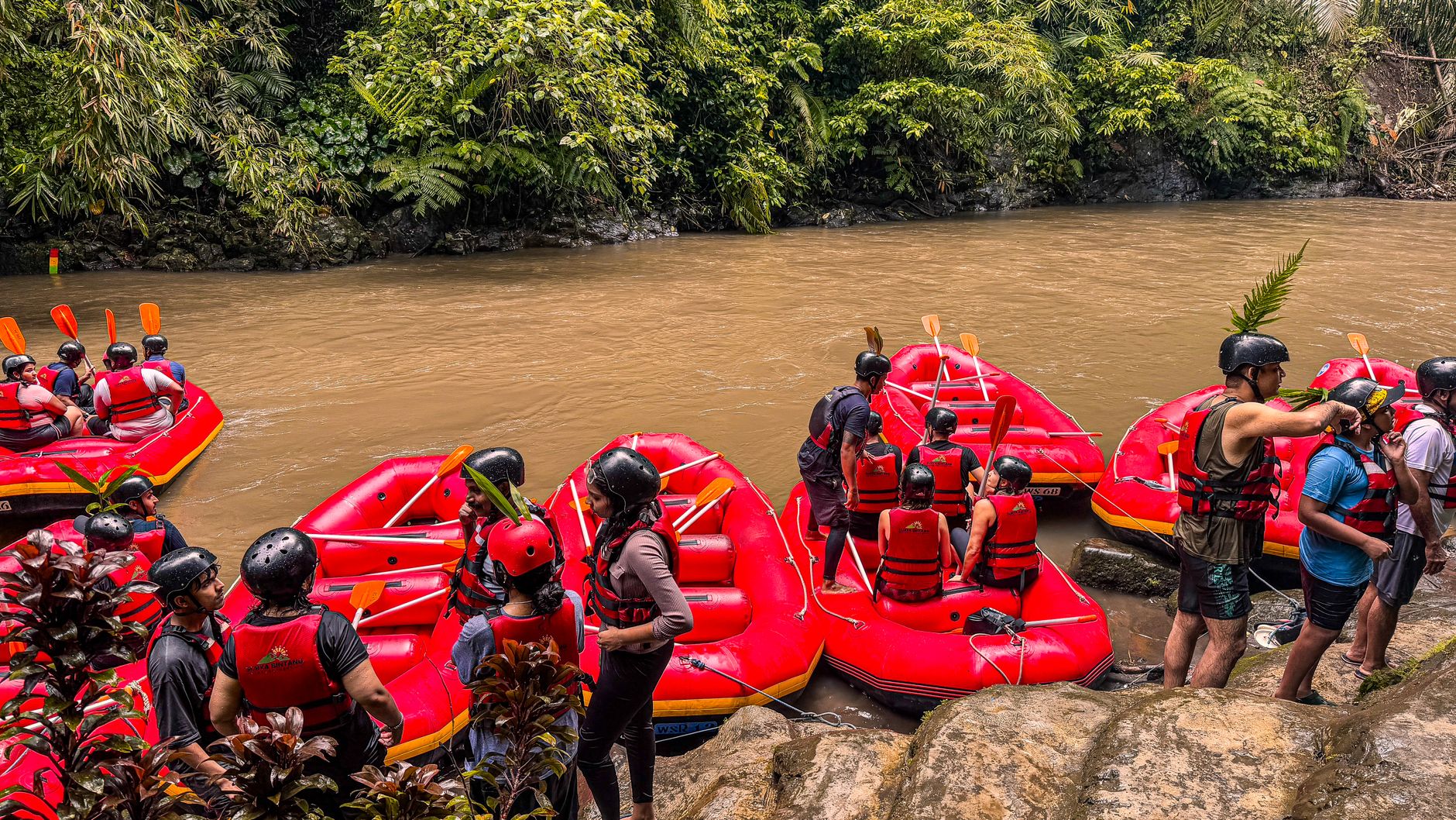 Group of people enjoying an exhilarating river rafting adventure with vibrant red rafts amidst lush greenery.