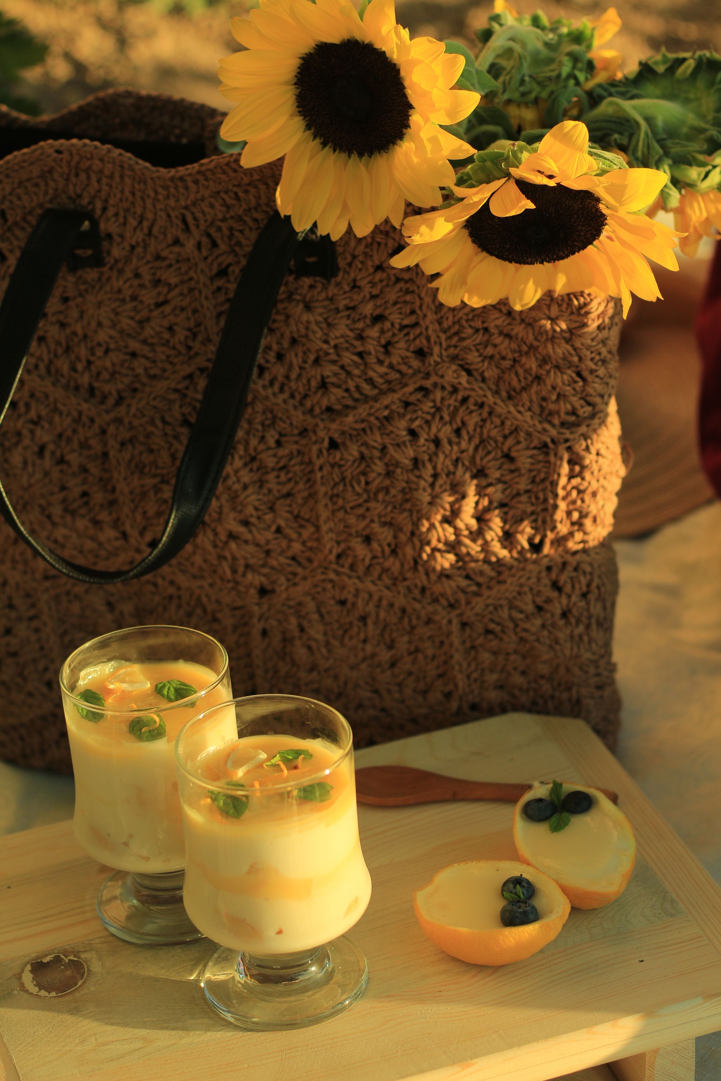 Sunlit picnic with sunflowers, glasses of dessert, and oranges for a fresh outdoor vibe.