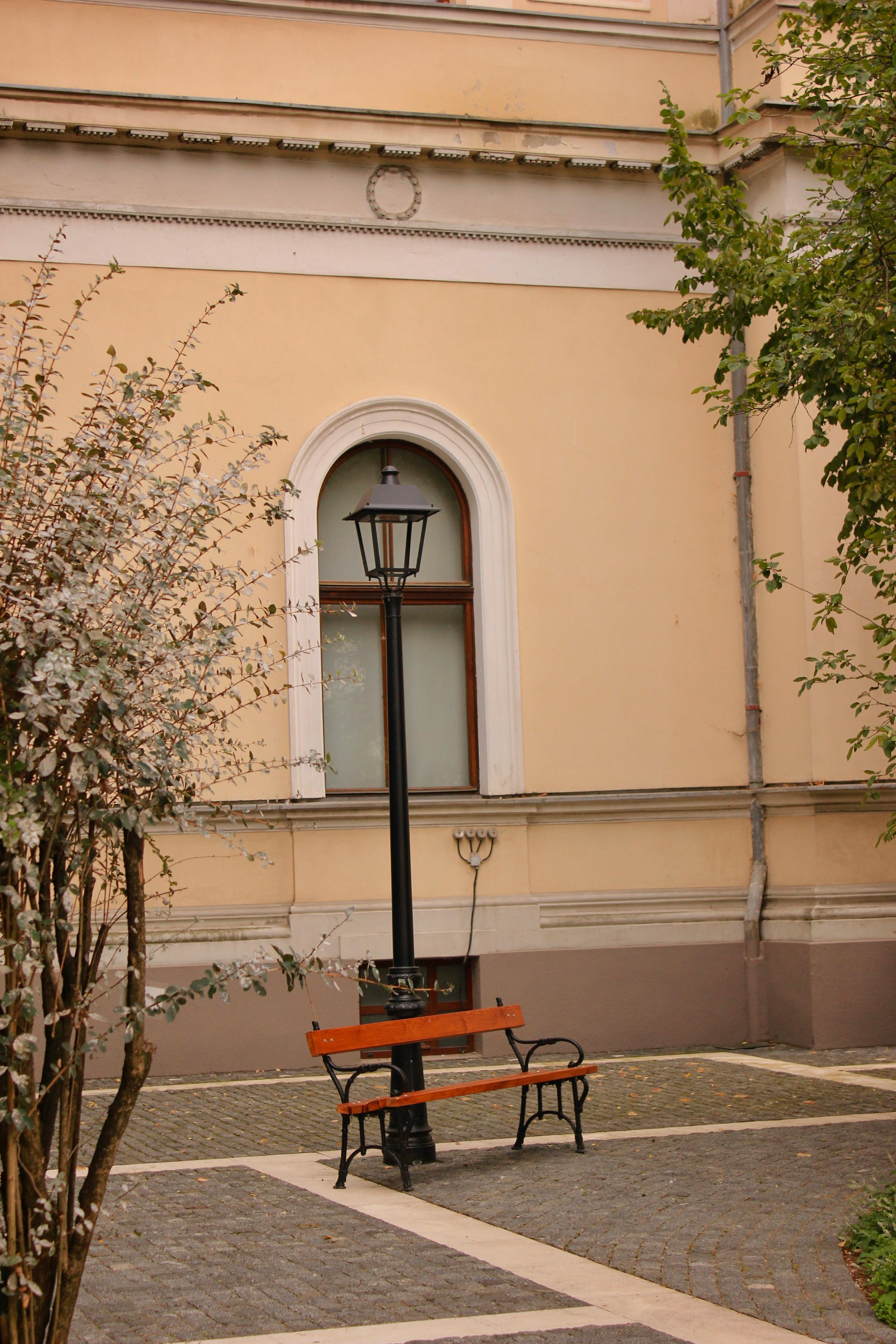 Bezpłatne Spokojny dziedziniec z ławką obok latarni, otoczony klasyczną architekturą. Zdjęcie z galerii