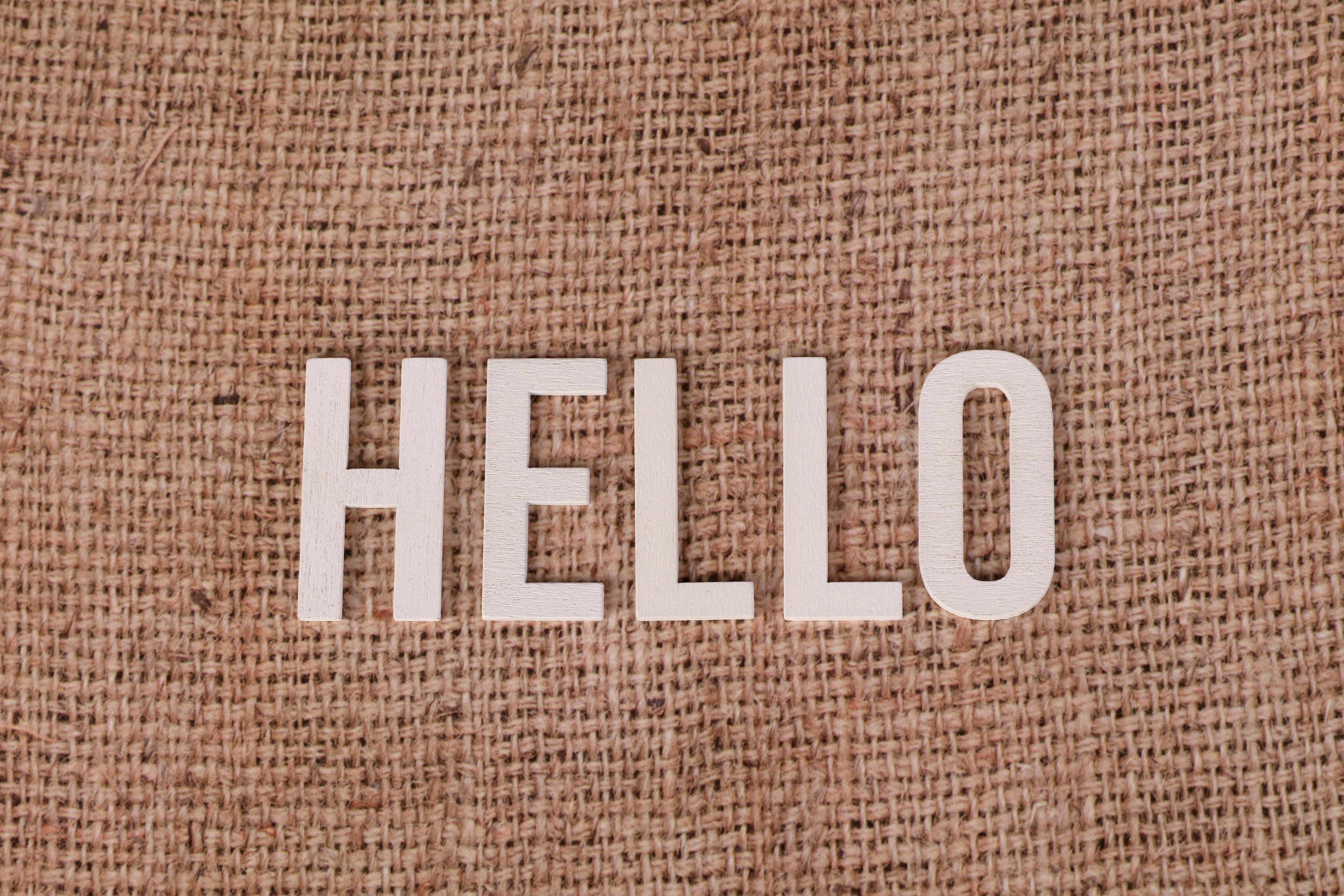 無料 素朴な黄麻布の背景に木製の文字で「HELLO」の文字が書かれ、温かい挨拶を伝えています。 写真素材