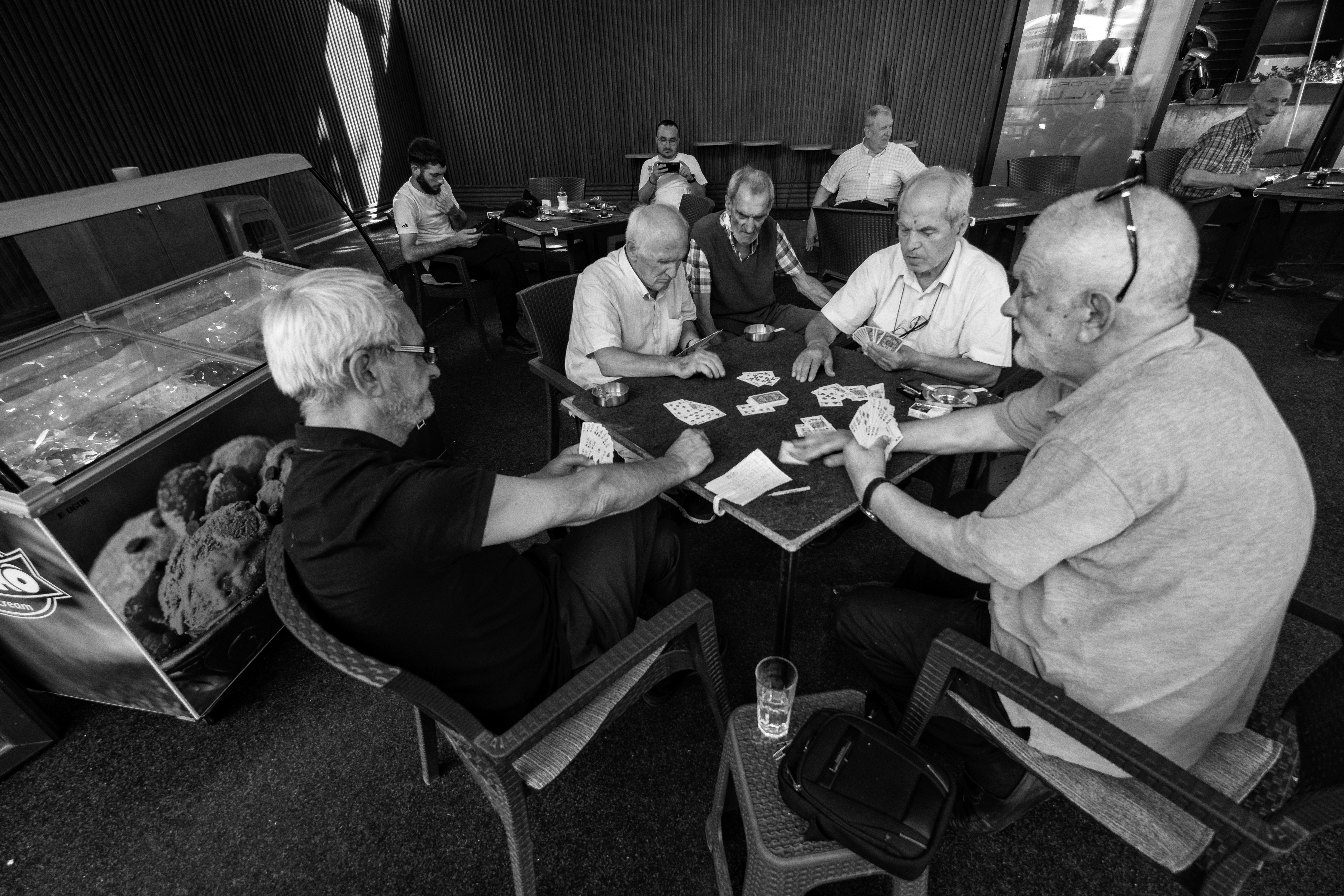 Black and white photo of senior men playing cards in a café in Üsküp, creating a relaxed and social atmosphere.