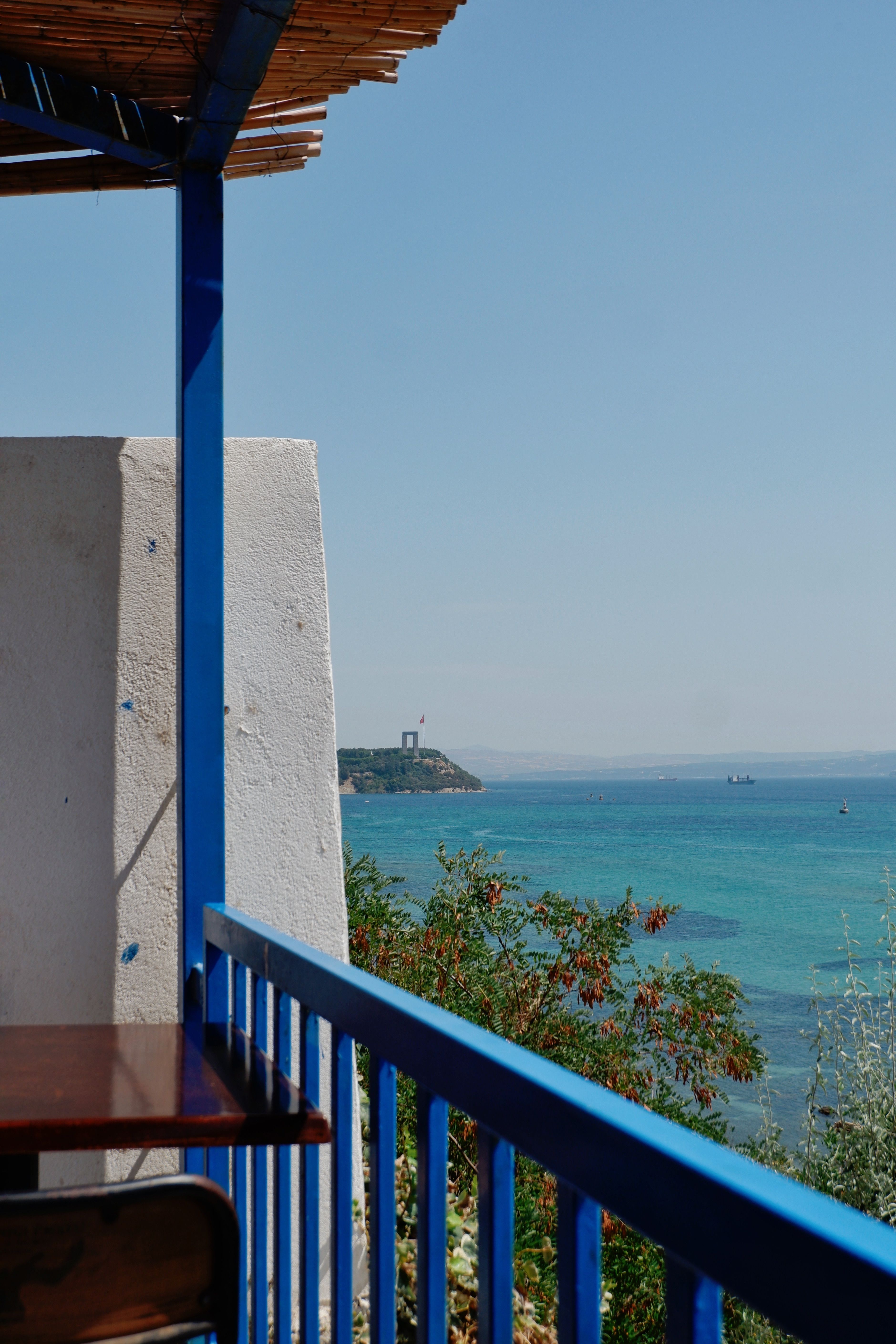 Tranquil seaside scene viewed from a balcony with vibrant blue railings, overlooking the ocean.