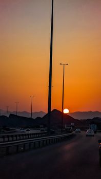 Sunset over a highway in Muscat, Oman, with stunning orange sky and mountains in the background.