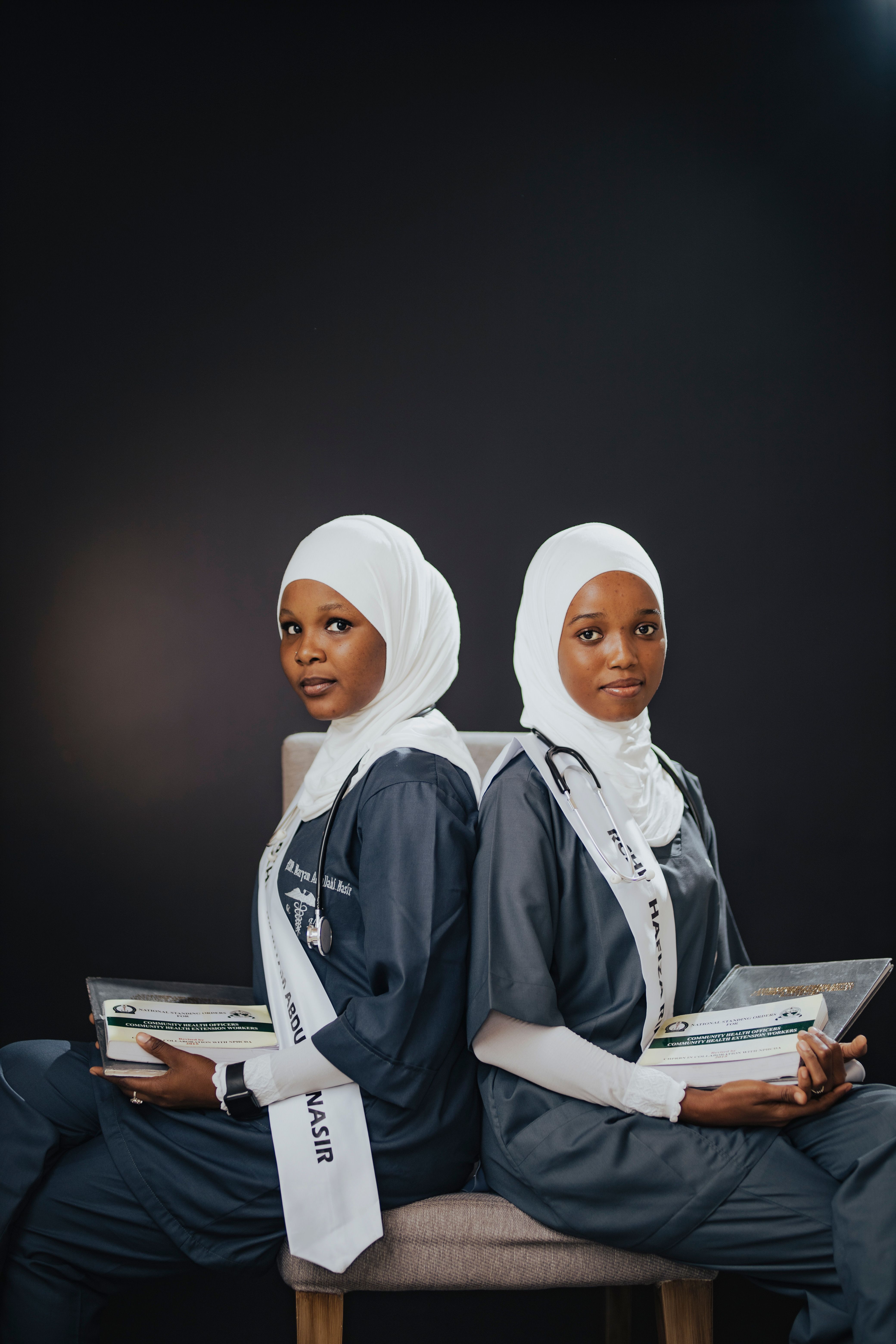 Two young female medical graduates in hijabs holding diplomas, celebrating their achievement.