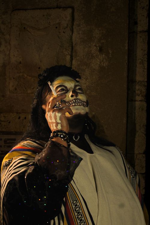 Free Person wearing skull makeup and costume looks up while smoking in a dimly lit setting. Stock Photo
