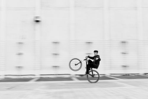 Free Black and white photo capturing a person performing a bicycle wheelie in an urban setting. Stock Photo