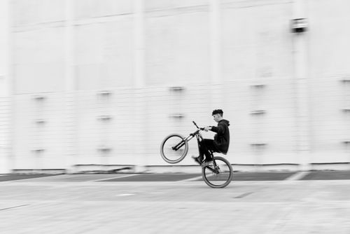 Free Black and white photo of a cyclist performing a wheelie in an urban setting. Stock Photo