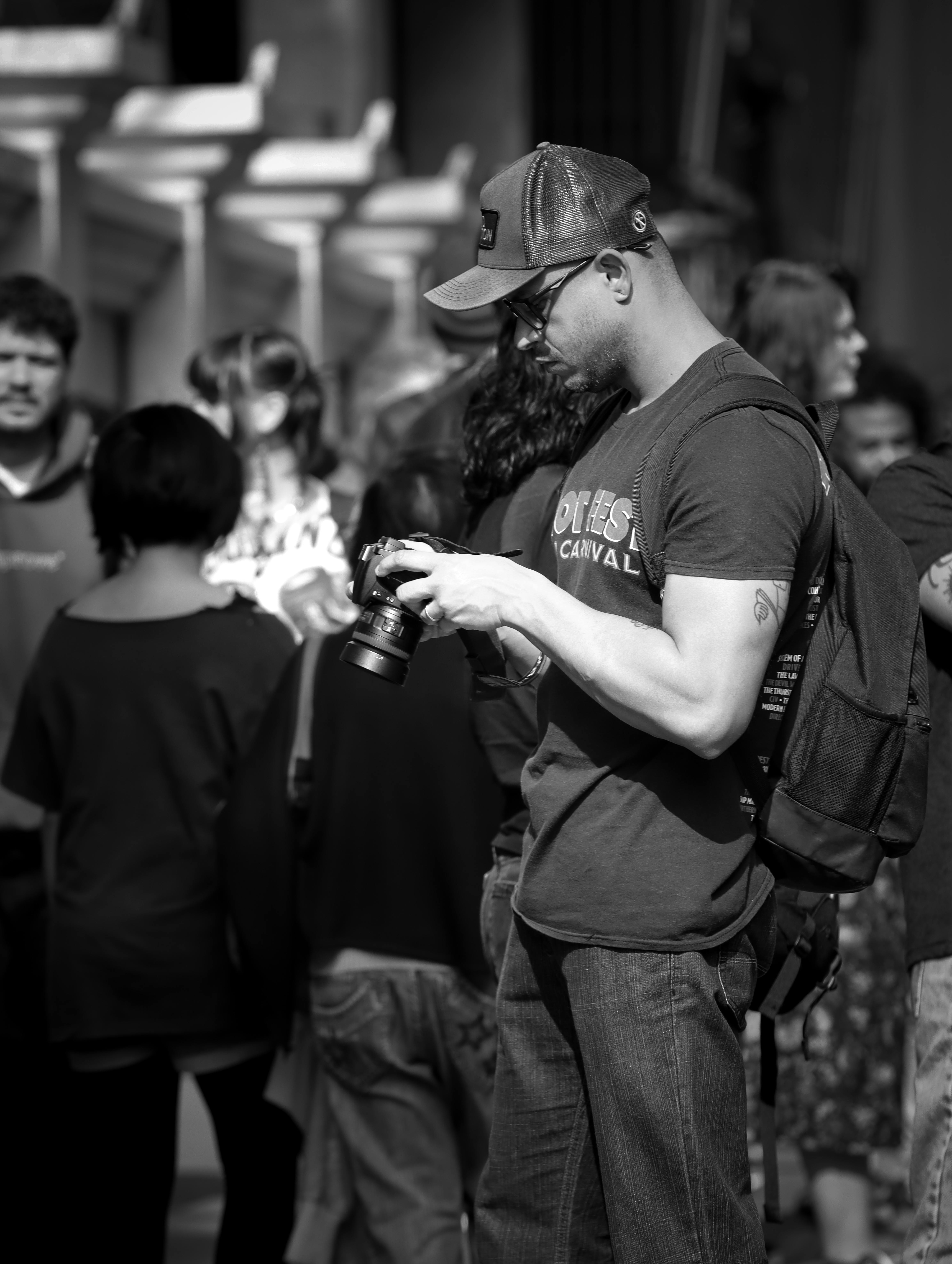 Street photographer focusing intently on camera amidst city crowd in black and white.