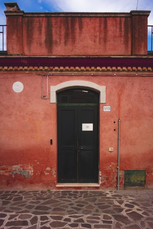 Free Charming rustic red facade with dark door and stone pathway. Stock Photo
