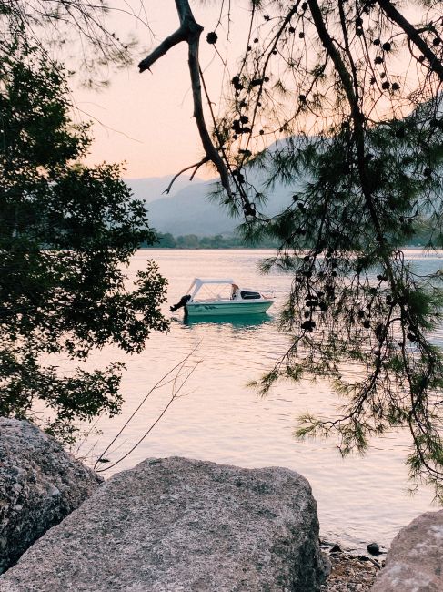 Serene view of a boat on a lake at sunset framed by trees and rocks.