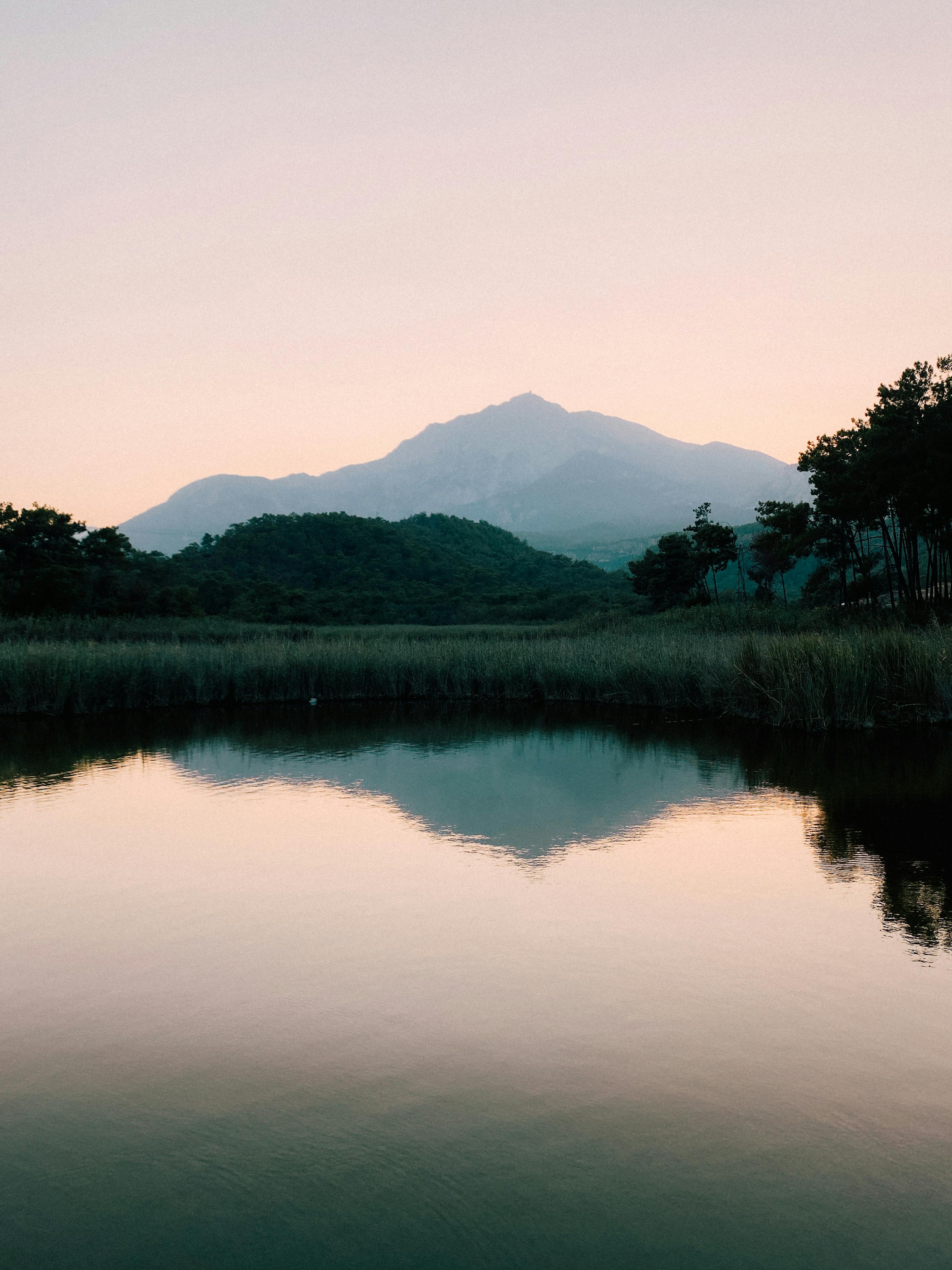 A tranquil scene of a mountain reflecting in a calm lake at sunset.