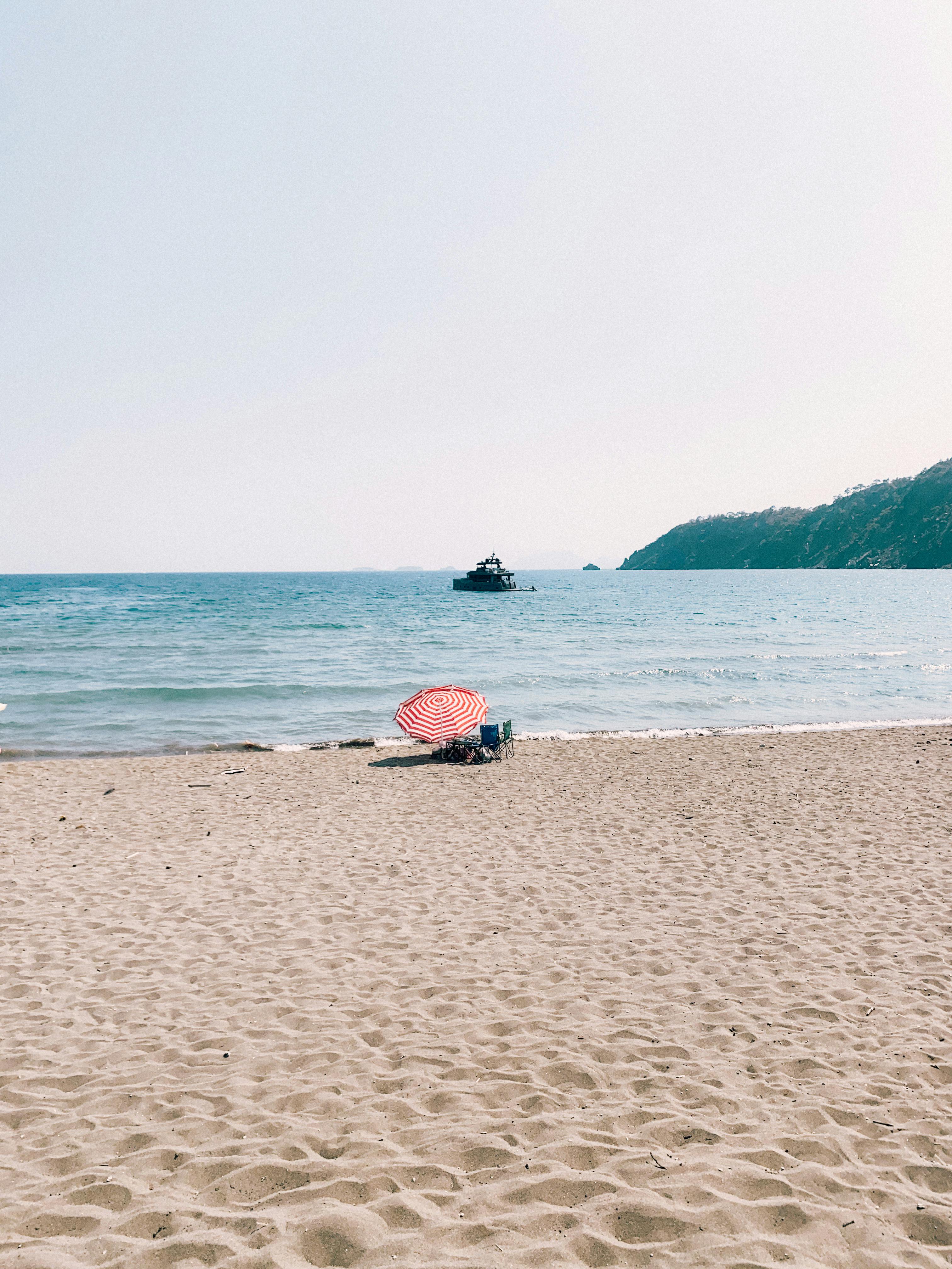 A tranquil beach scene in Antalya with a lone umbrella and boat in the distance.