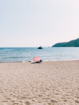 A tranquil beach scene in Antalya with a lone umbrella and boat in the distance.