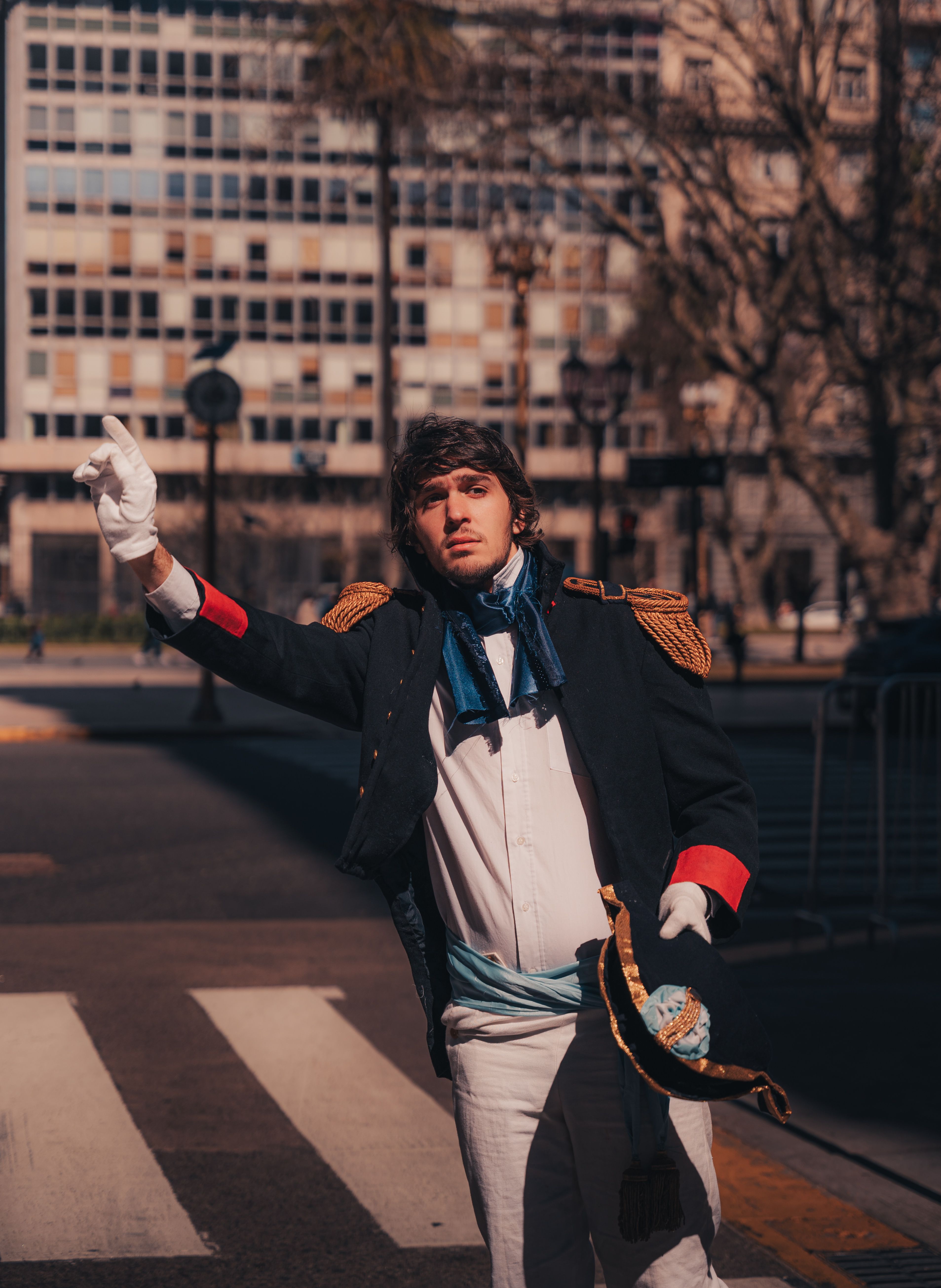 A young adult dressed in a historical military costume poses outdoors on a sunny day.