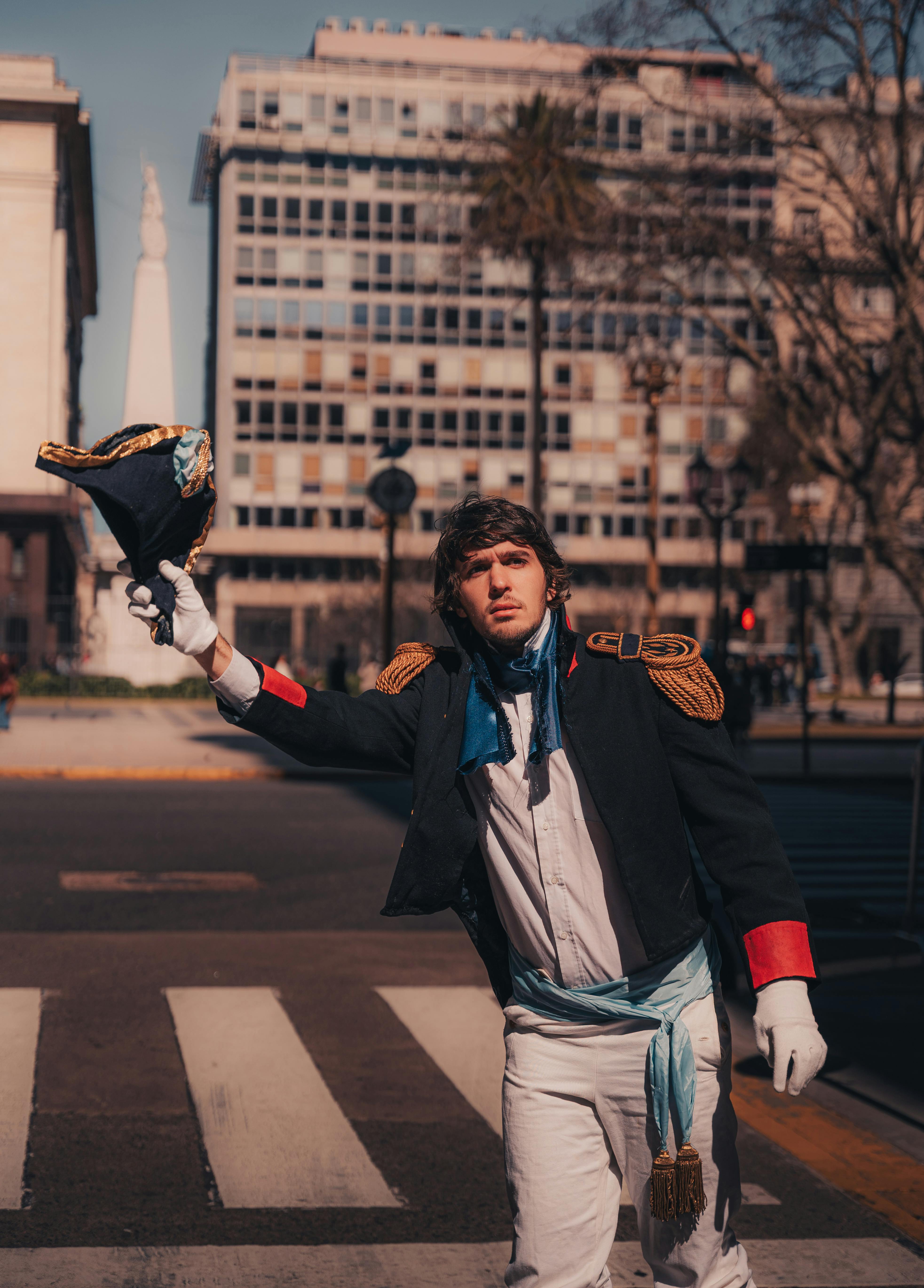 Person in historical soldier costume raising hat on city street. Urban background with warm daylight.