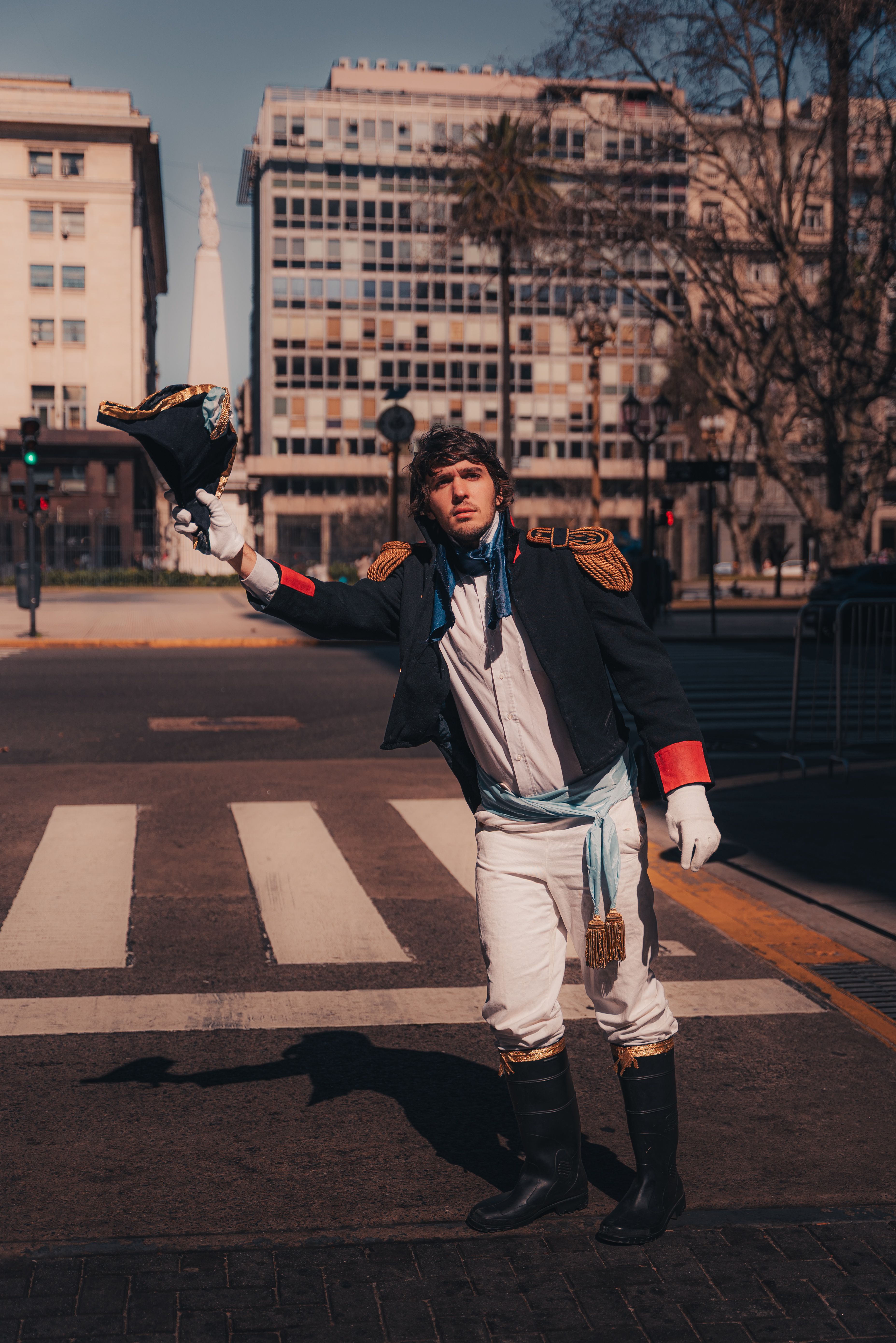 A historical reenactor in period soldier costume posing with a hat in an urban setting.