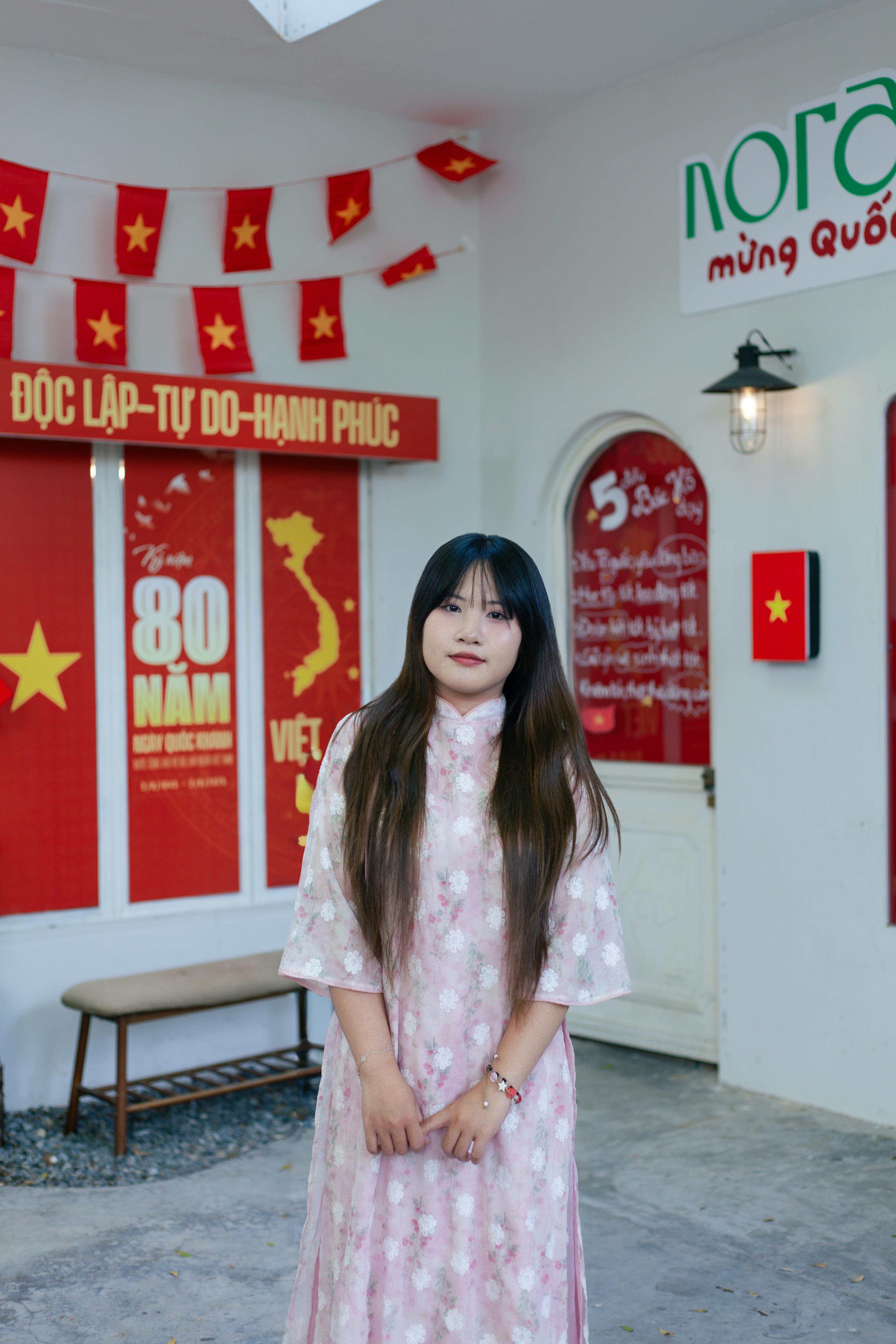 Asian woman in traditional dress indoors with Vietnamese flags and festive decorations, symbolizing cultural heritage.